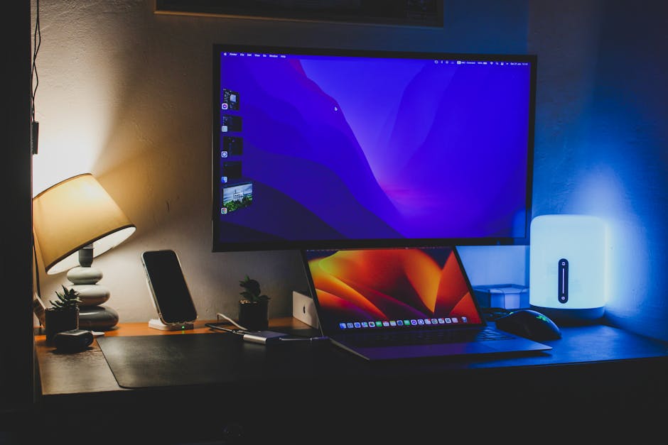 A cozy home office desk featuring a laptop, monitor, lamp, and indoor plants, creating a productive environment.