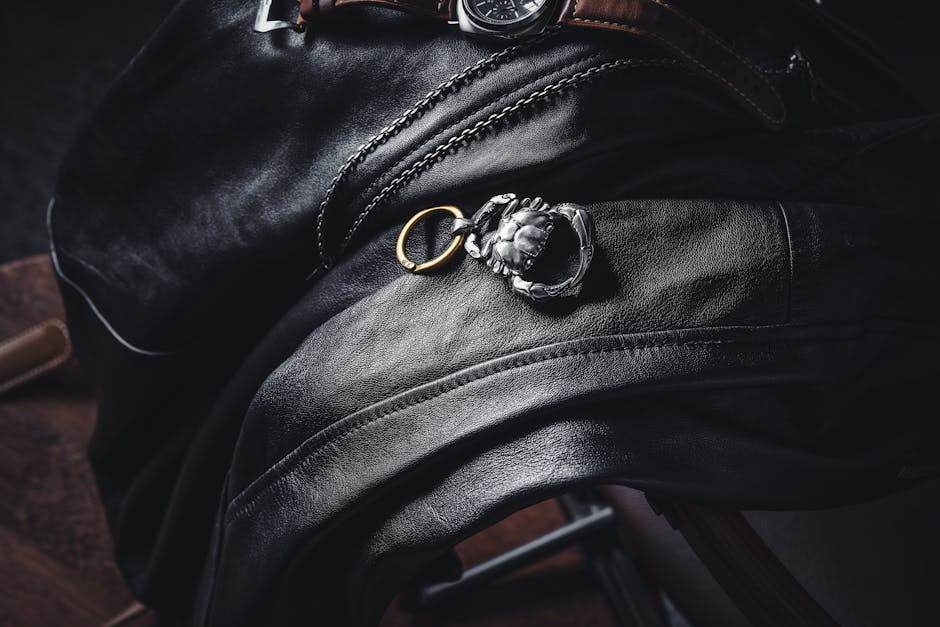 Stylish leather draped with a silver keychain and wristwatch in a moody setting.